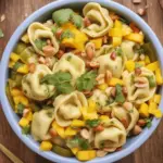 Sommerlicher Tortellini-Mango-Salat mit Limettendressing auf einem Teller angerichtet.