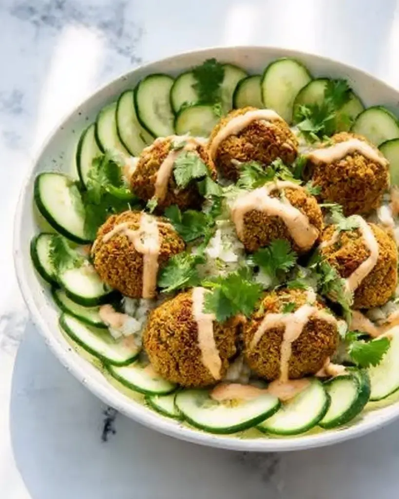 Baked lentil split pea falafel bowl with tahini dressing, garnished with fresh vegetables.
