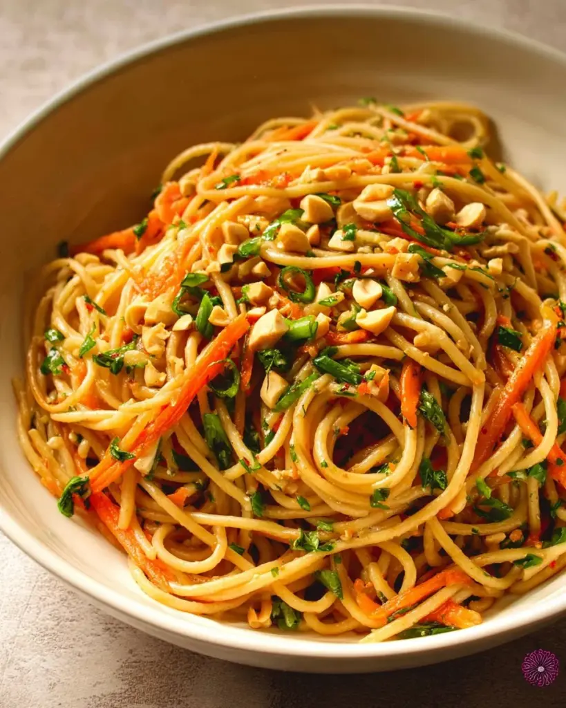 Bowl of creamy peanut noodles garnished with cilantro and peanuts