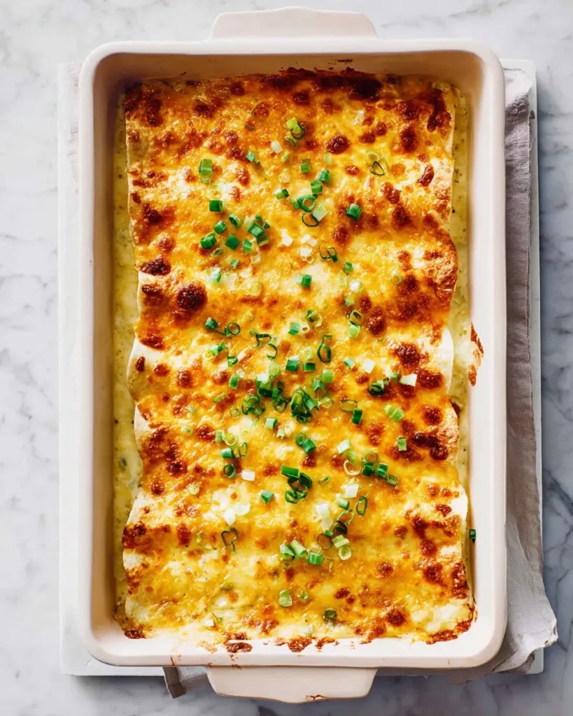 Cheesy chicken enchiladas topped with creamy white sauce and garnished with cilantro.